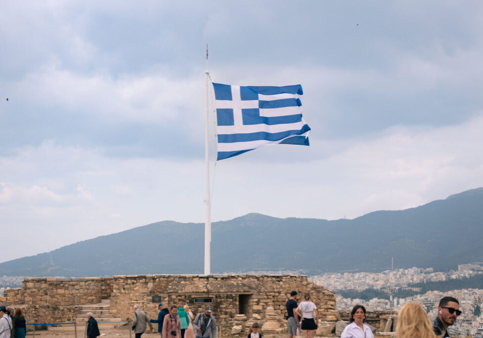 The national Greek flag flying at full mast on top of the Acropolis, Athens with mountains in the distance