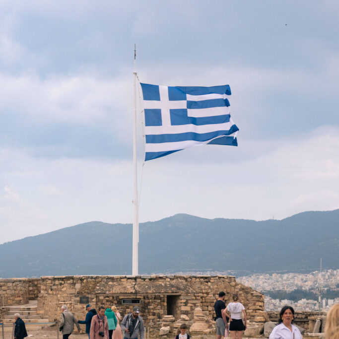 The national Greek flag flying at full mast on top of the Acropolis, Athens with mountains in the distance